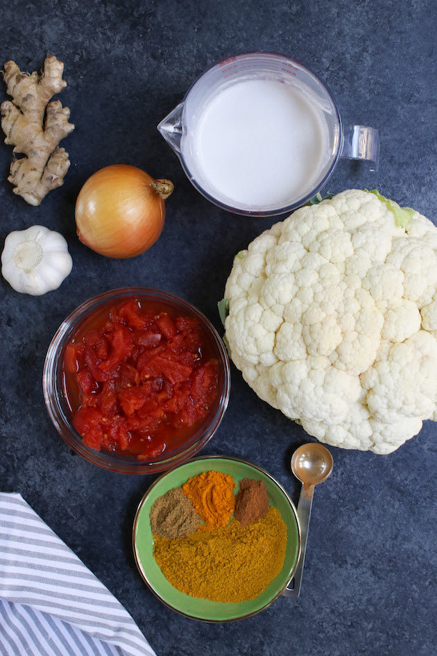 All ingredients displayed on the counter: coconut milk, cauliflower, ginger, onion, garlic, diced tomatoes, yellow curry powder, turmeric, cinnamon and cumin
