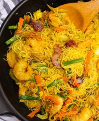 Singapore chow mei fun in a skillet showing thin rice noodles, shrimp, pork and vegetables in a characteristic yellow color
