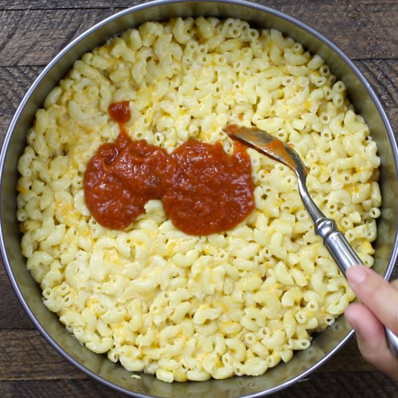 Spooning sauce on top of the mac and cheese crust