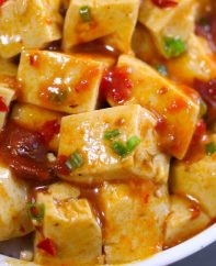 Mapo Tofu served in a rice bowl topped with crushed szechuan peppercorns and minced green onions