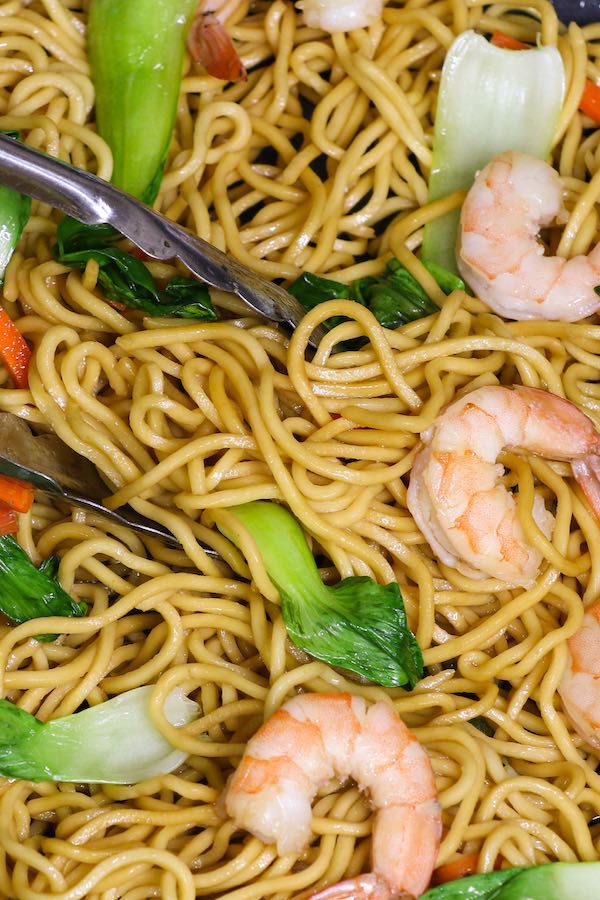 Closeup of tongs picking up noodles with shrimp and bok choy
