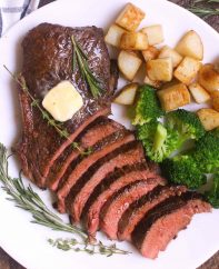 Overhead view of a sirloin steak dinner consisting of sliced top sirloin garnished with fresh rosemary, thyme and a pat of butter, served with sautéed potatoes and broccoli