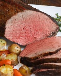 Slices of sirloin tip roast on a serving plate with roasted potatoes and carrots