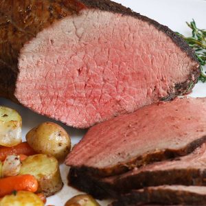 Slices of sirloin tip roast on a serving plate with roasted potatoes and carrots