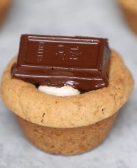 S’mores Cookie Cups – The perfect s’mores recipe that’s one of my favorite! Hot Graham cracker cookie cups baked in mini muffin tin, filled with marshmallow, and then topped with semi-sweet Baker’s or Hershey’s chocolate bars, boiled to gooey perfection. They melt in your mouth! So Yummy! All you need is only a few simple ingredients. Fun recipe to make with kids. Quick and Easy recipe that takes only 25 minutes. Dessert, Party Food. Vegetarian. Video recipe. | Tipbuzz.com