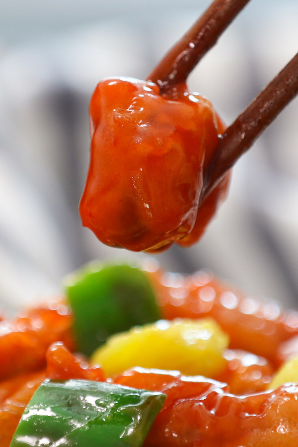 A piece of Sweet and Sour pork being picked up with chopsticks