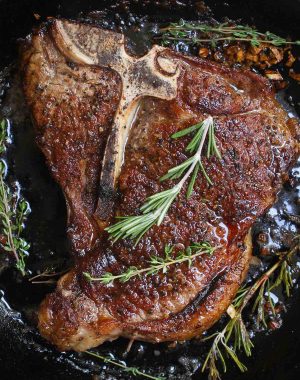 T-bone steak searing in a hot cast iron skillet