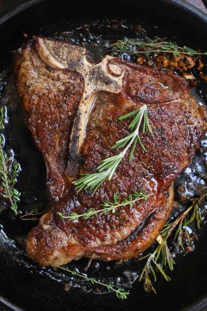 T-bone steak searing in a hot cast iron skillet