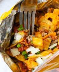 Closeup of a walking taco made with Fritos, ground beef, cheese and onions, served out the bag of chips and eaten with a fork