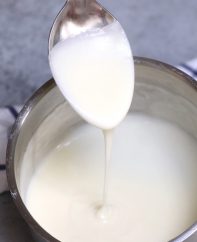 Spooning homemade white cheese sauce in a saucepan